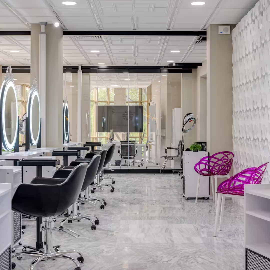Elegant beauty academy interior with white salon chairs, gold-framed mirrors, wooden flooring, and warm lighting, creating a welcoming and professional environment.